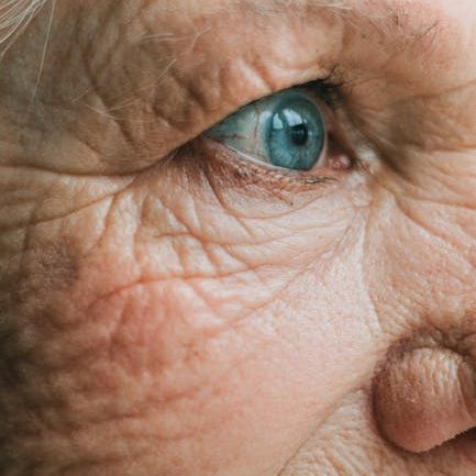 Detailed close-up shot of an elderly woman's blue eye, emphasizing wrinkles and aged skin texture.